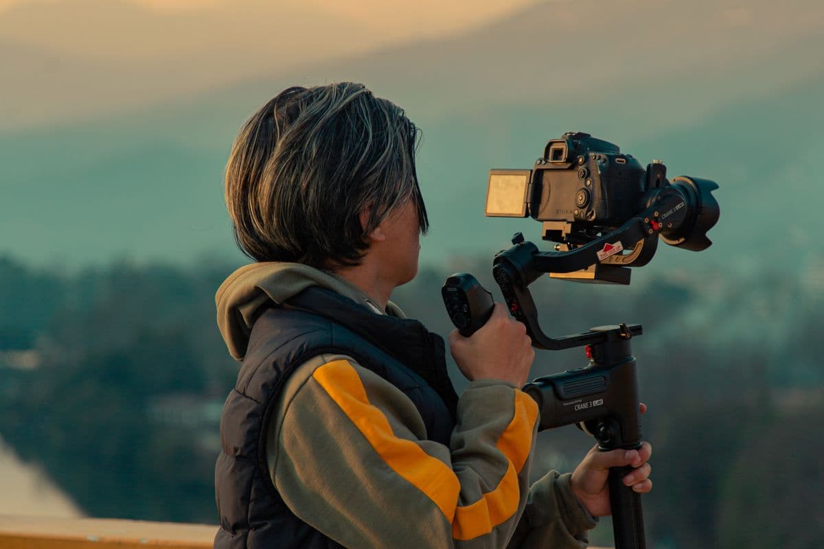 A creator filming a mountain landscape at dusk with a camera on a gimbal.