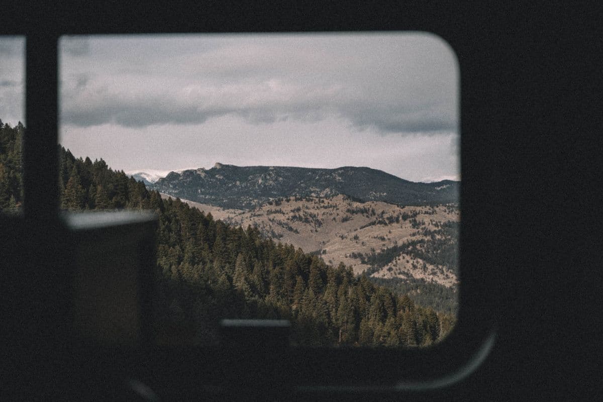 Un paisaje montañoso pasando por la ventana de un tren durante un viaje largo.