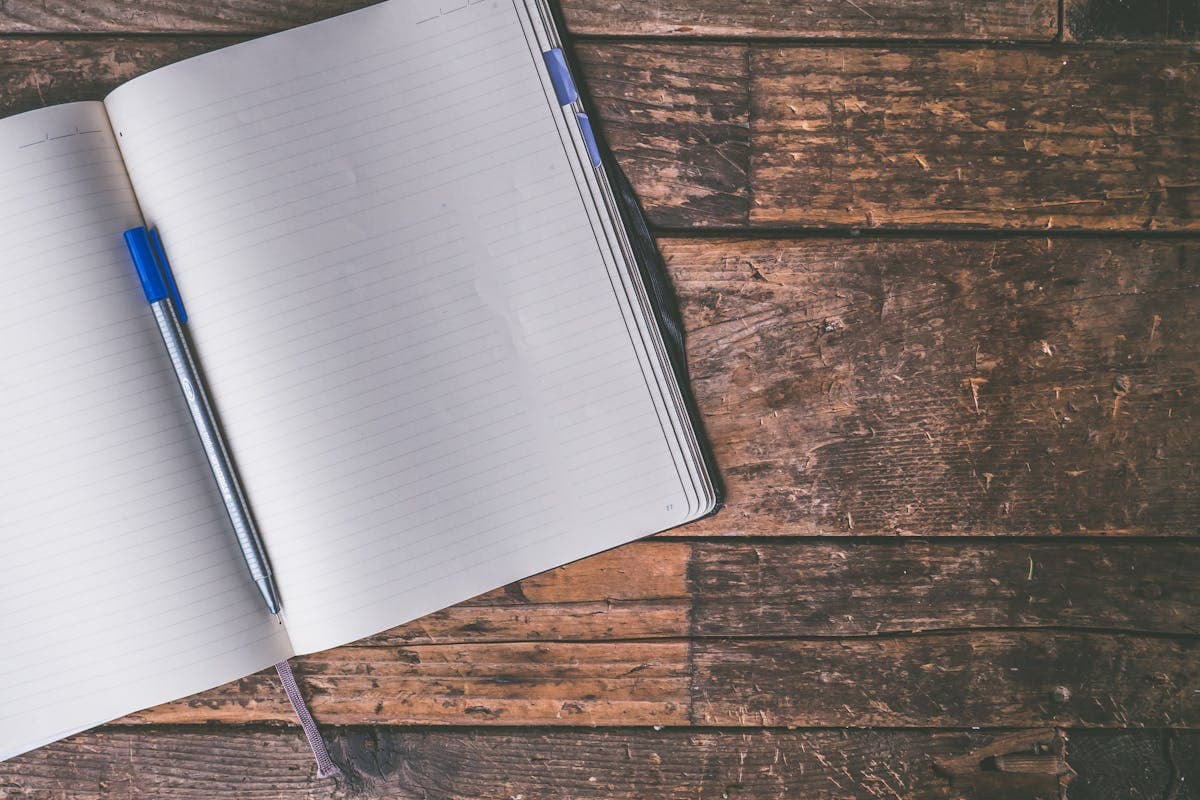 Un cuaderno abierto y un bolígrafo sobre un escritorio, listos para una entrada del diario de viaje.