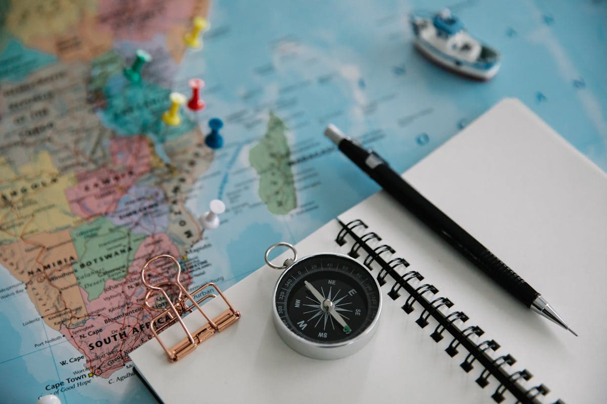 Un cuaderno junto a un mapa del mundo con pines, los primeros pasos de un plan de viaje.