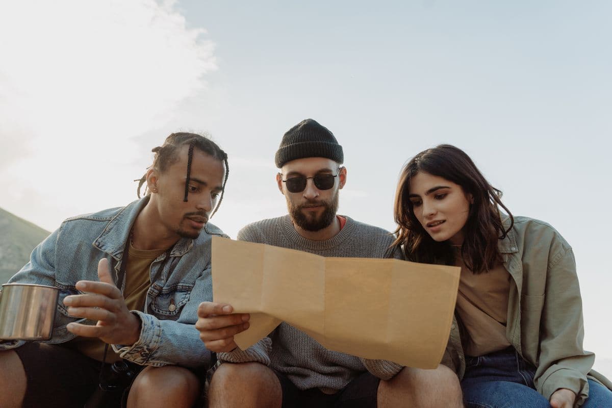 Three friends reading a paper map together outdoors, planning where to go next.