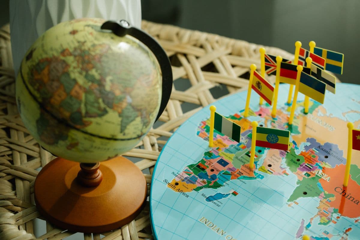 Un globo terráqueo junto a un mapa plano del mundo con pequeños marcadores de banderas de países.